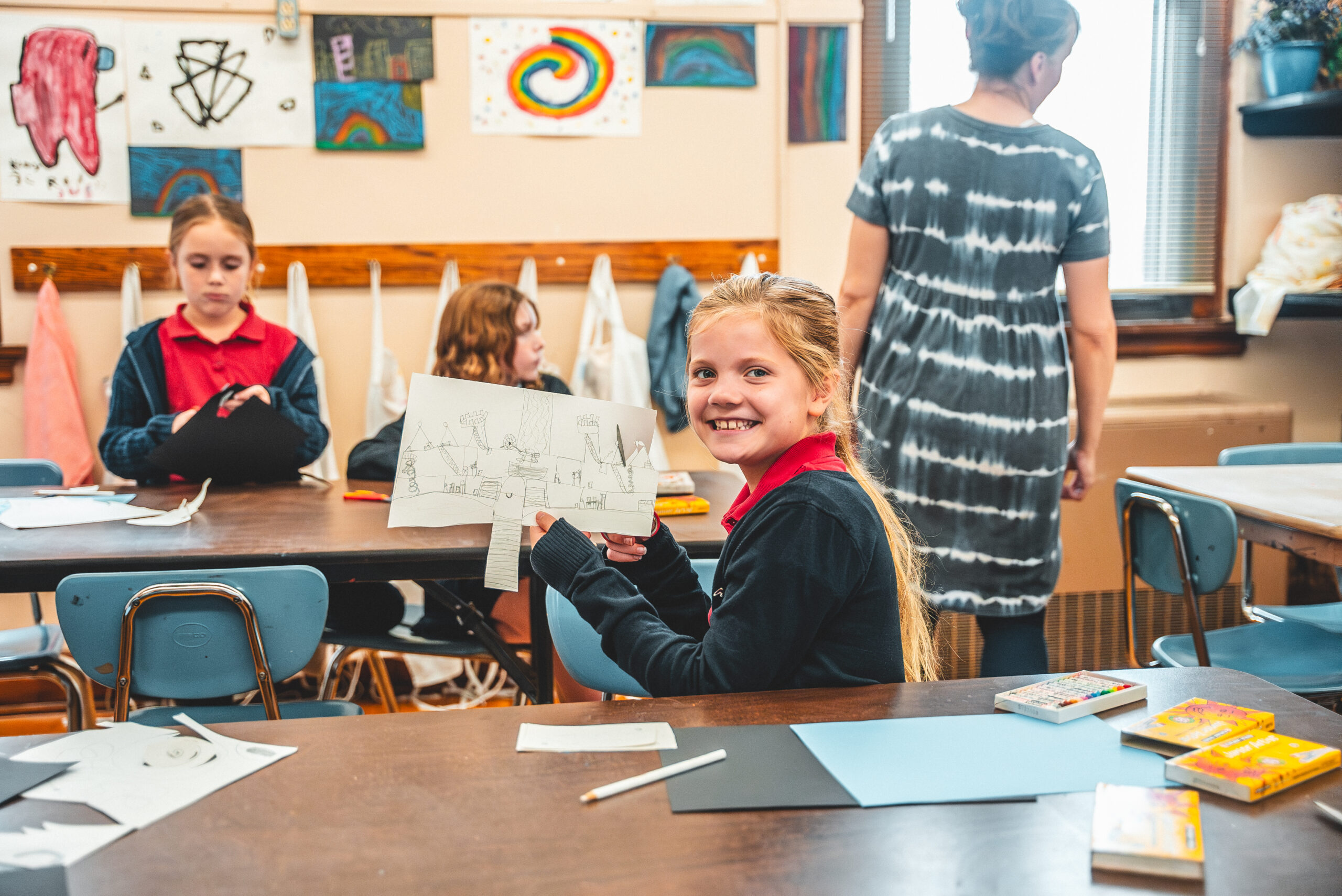 A smiling St. Francis student holding up her drawing in art class
