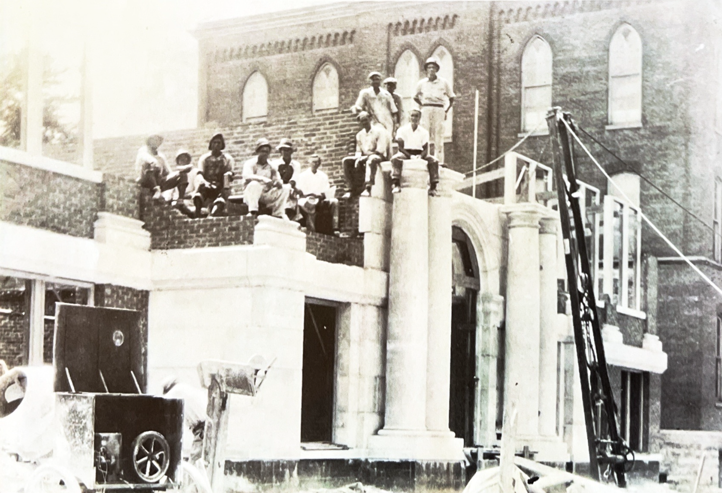 Workmen seated on the unfinished front steps and stone columns of the new St. Francis school
