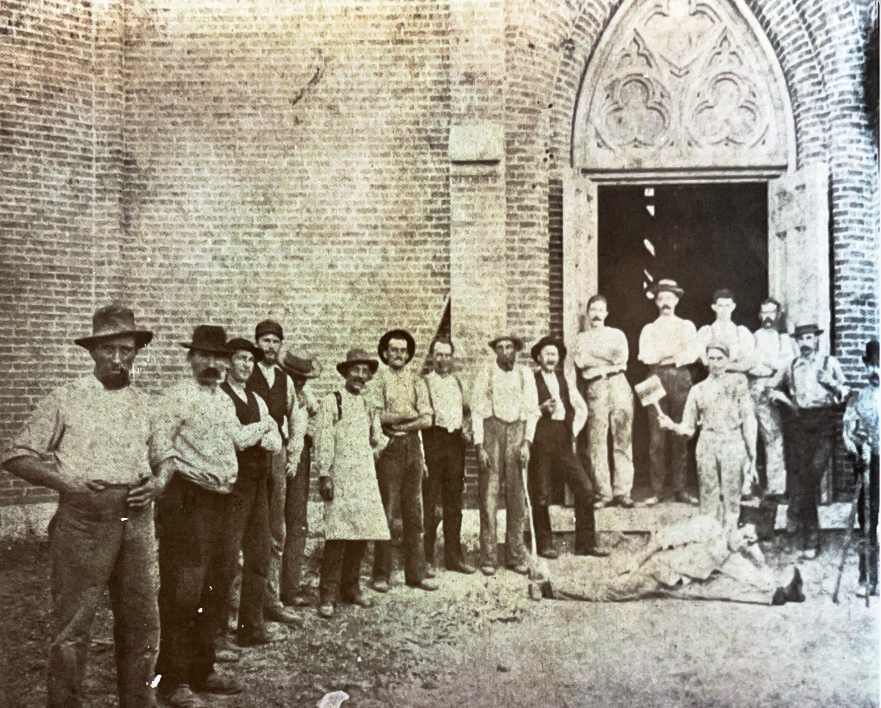 A line of workmen in shirtsleeves and hats standing at the Gothic doors of St. Francis Solanus Church