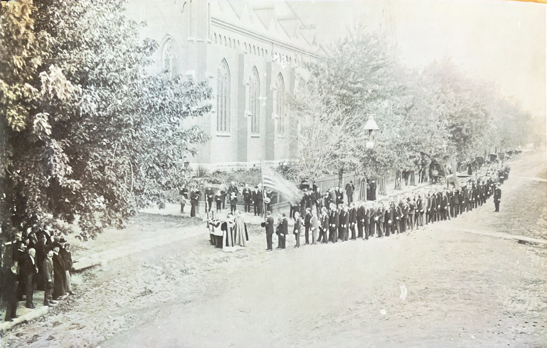 A long parish procession winding along the street beside St. Francis Solanus Church, in an old photograph