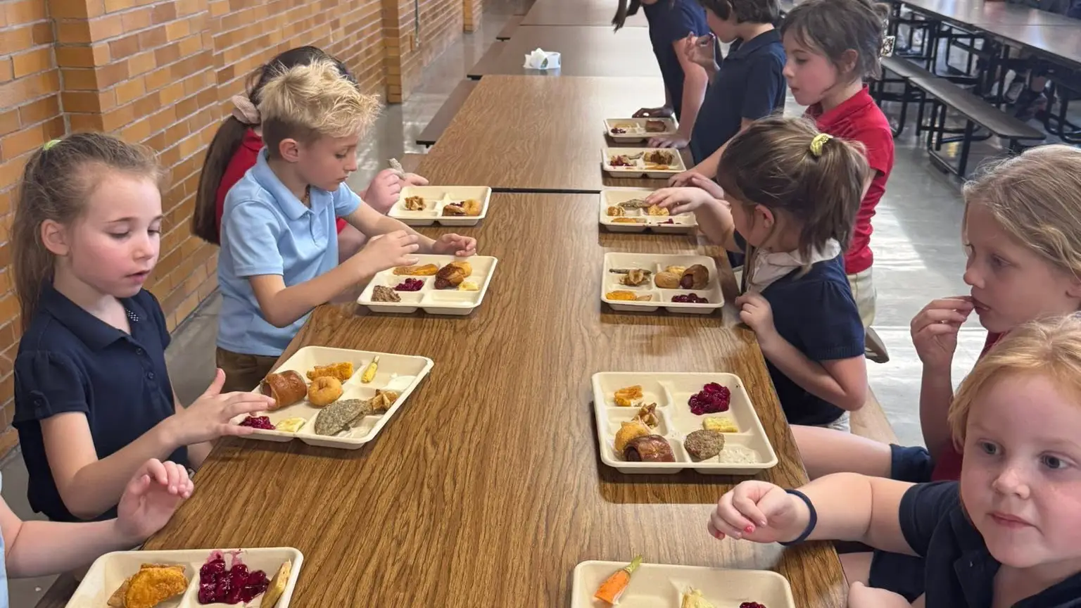 Young St. Francis students eating hot lunch together at a long cafeteria table