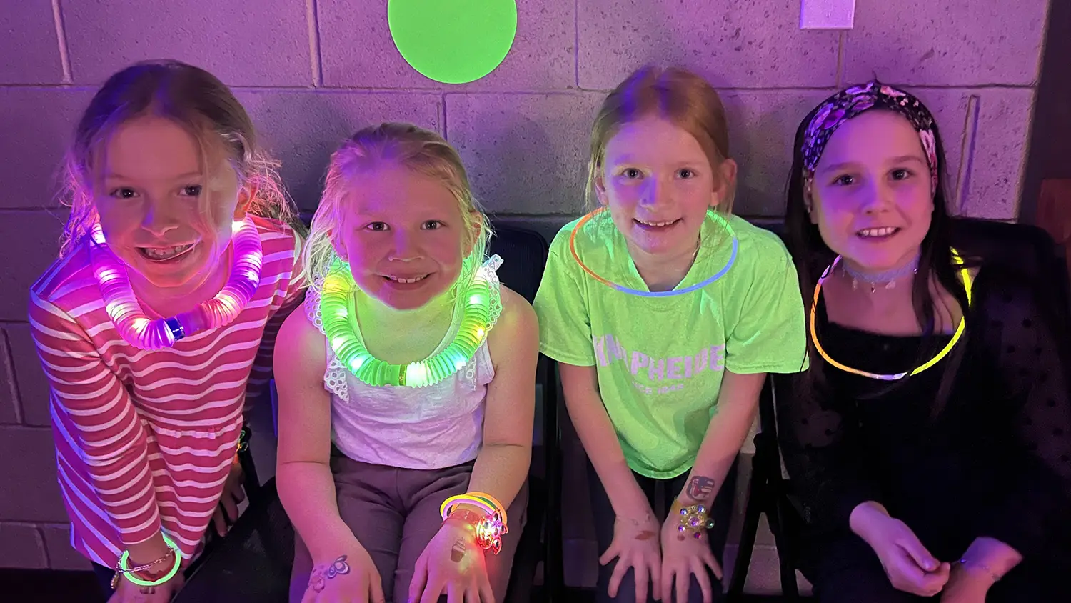 Four smiling students wearing glow necklaces and bracelets at a school dance