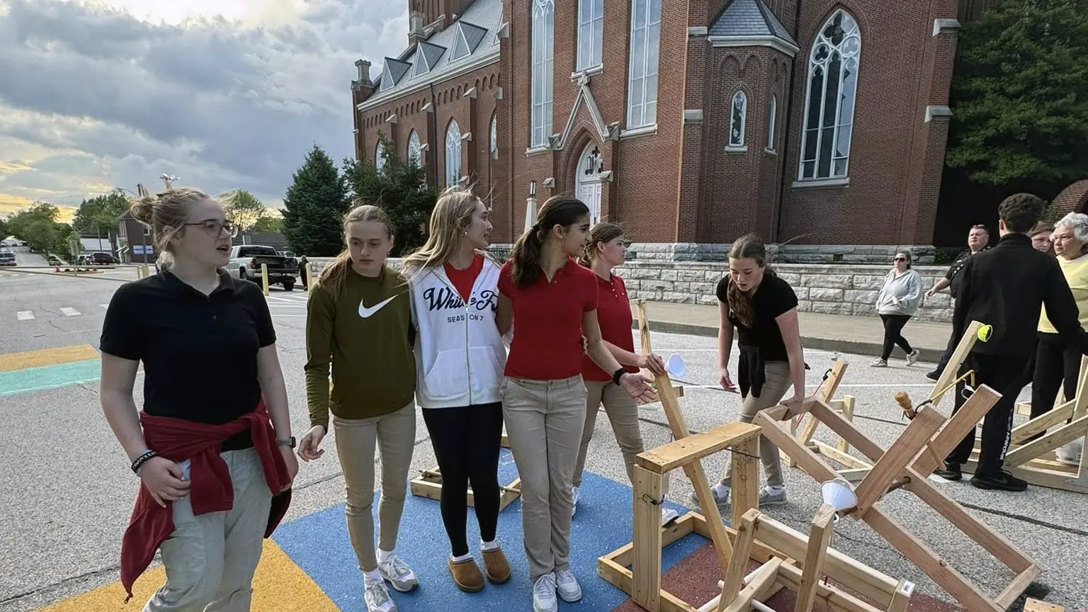 St. Francis students demonstrating wooden catapults they built, outside in front of the church