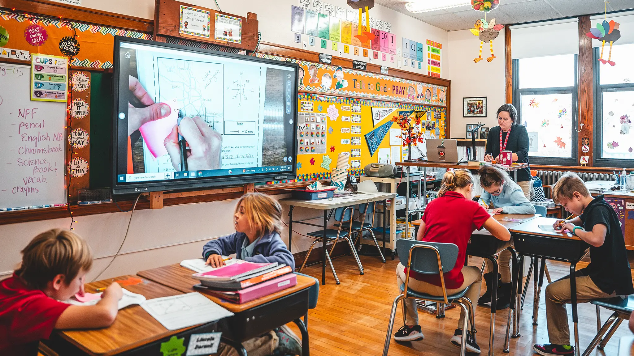 St. Francis students working at their desks while a teacher helps in a bright classroom