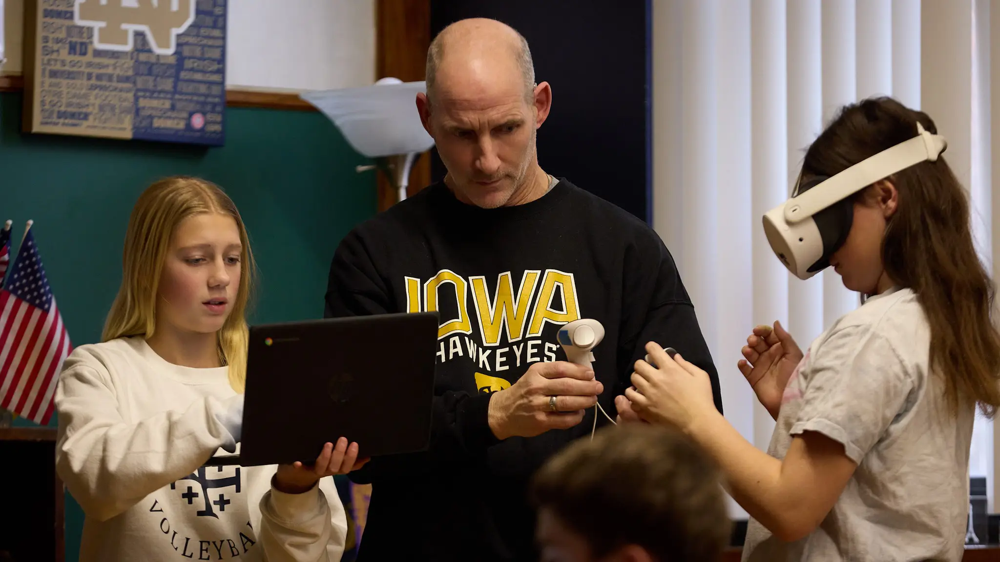 A St. Francis teacher helping a student with a virtual reality headset while a classmate works on a tablet