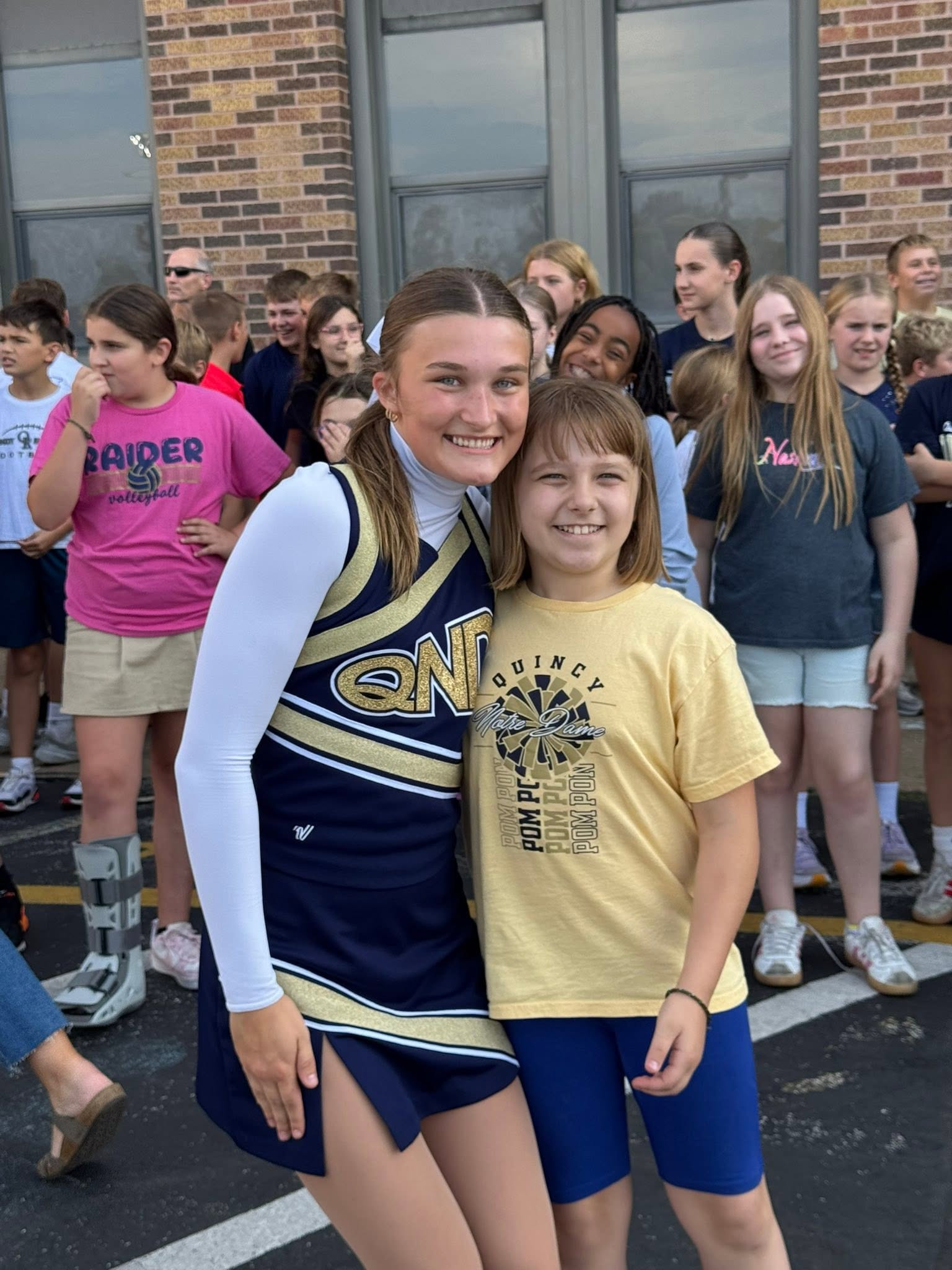 A Quincy Notre Dame cheerleader hugging a younger student in a Quincy pom shirt