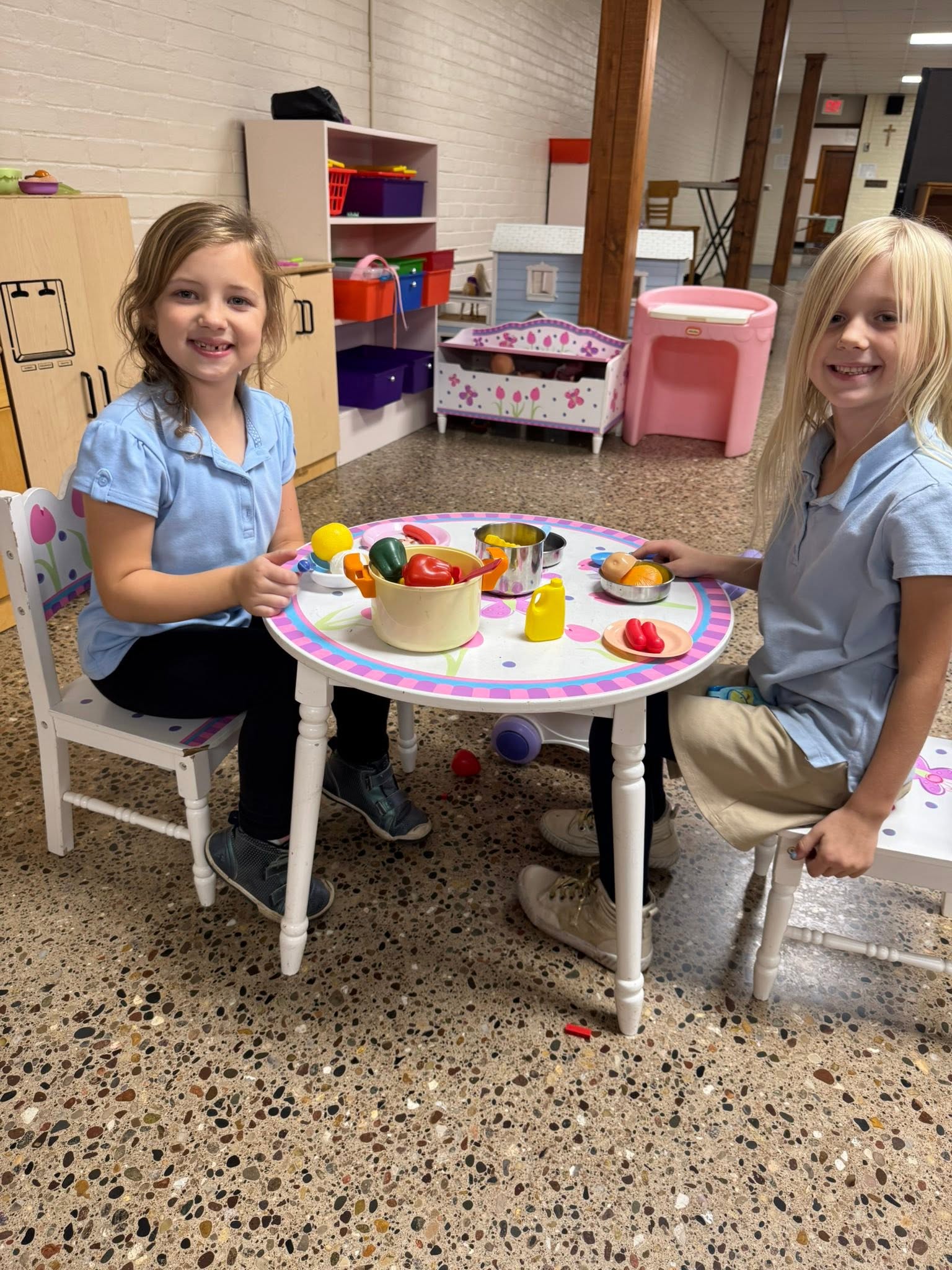 Two young St. Francis students smiling at a play kitchen table with toy food