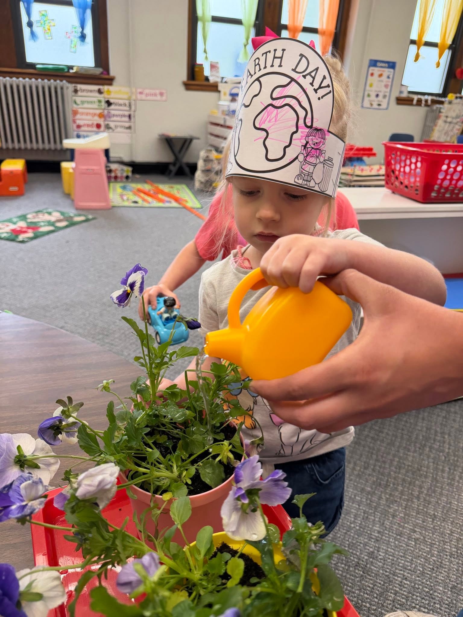 A St. Francis preschooler in a paper Earth Day crown watering potted pansies