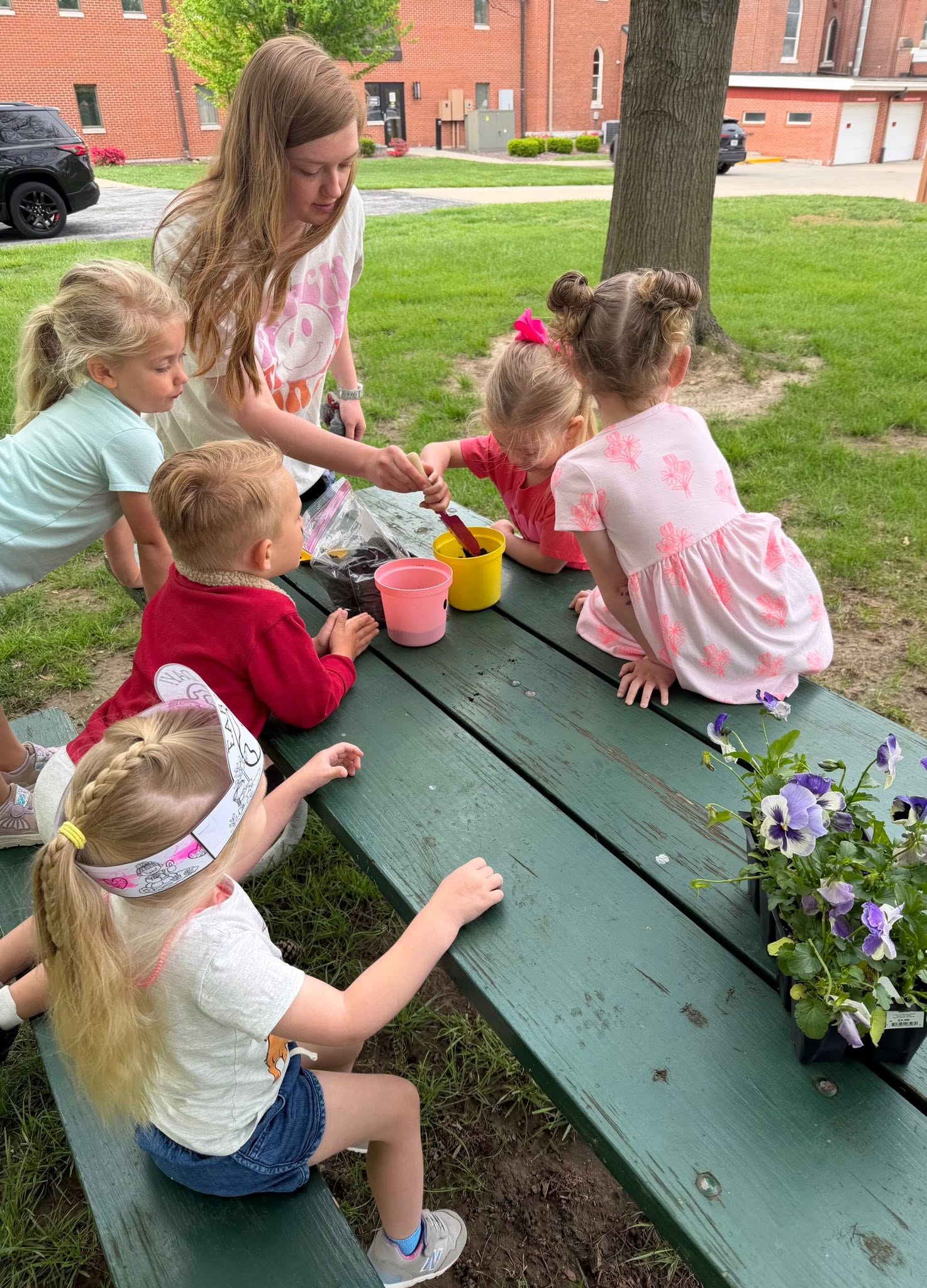A St. Francis preschool teacher planting flowers with her class at a picnic table outside