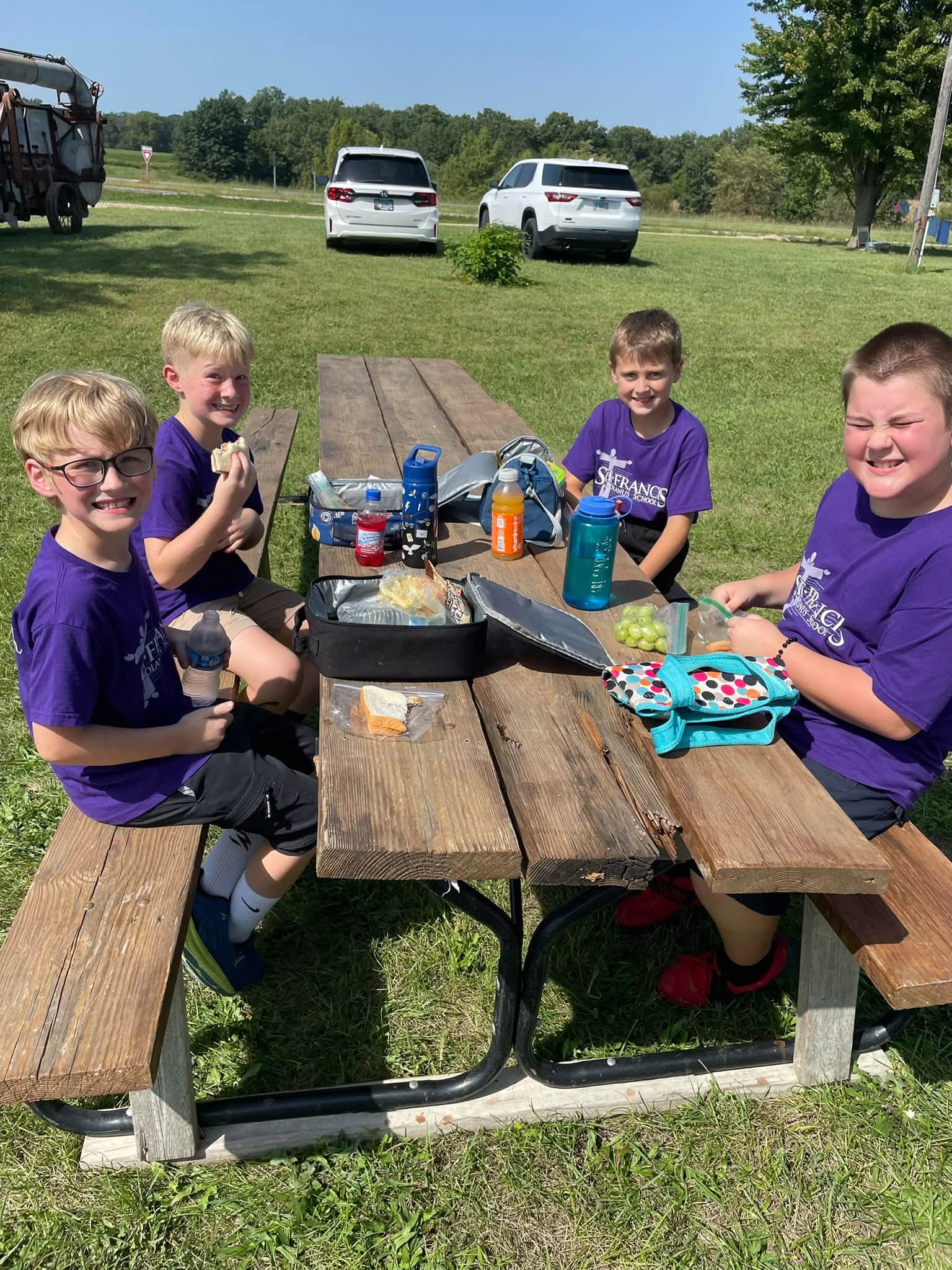 St. Francis students in purple school shirts eating lunch together at a picnic table outside