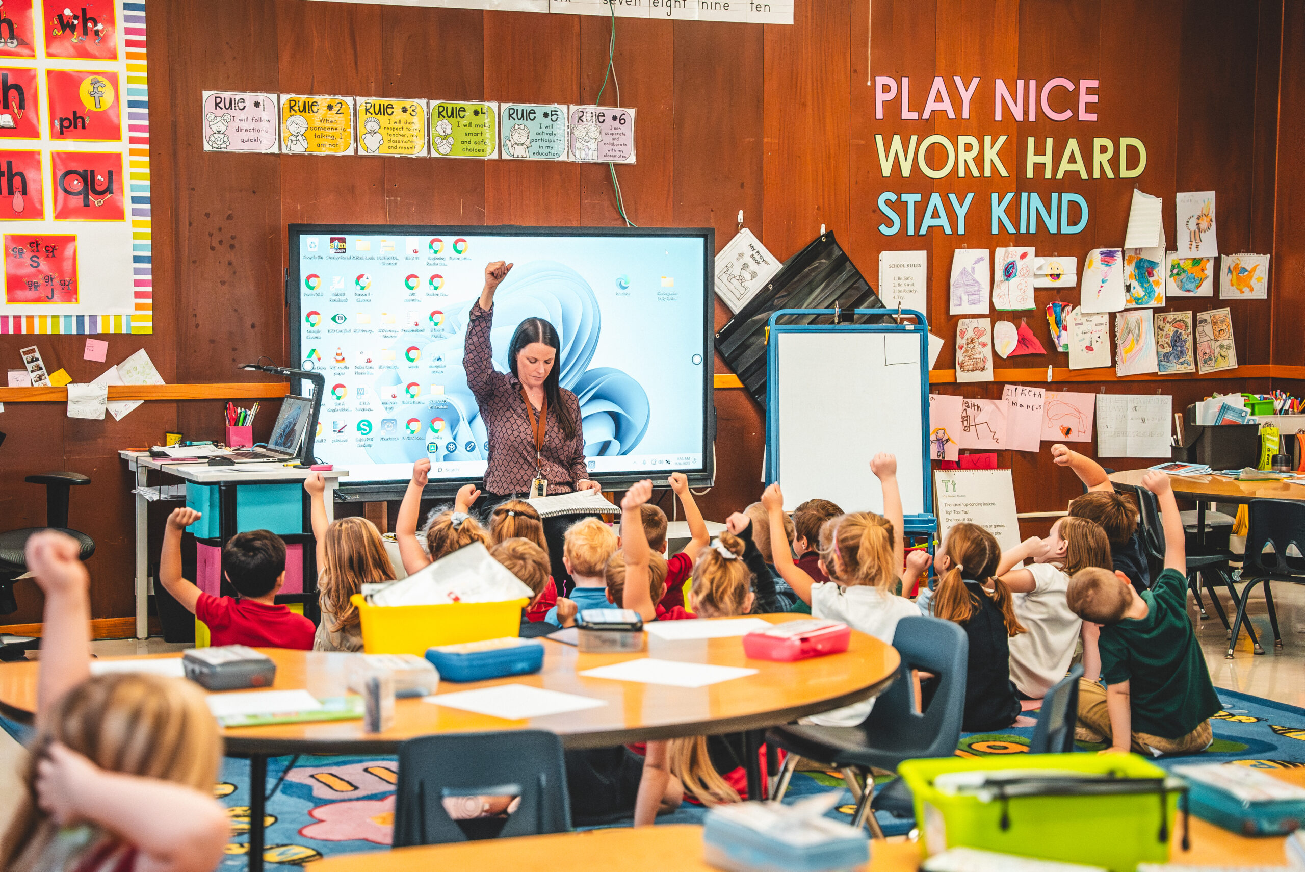 A St. Francis teacher leading a lesson at the smart board as young students raise their hands