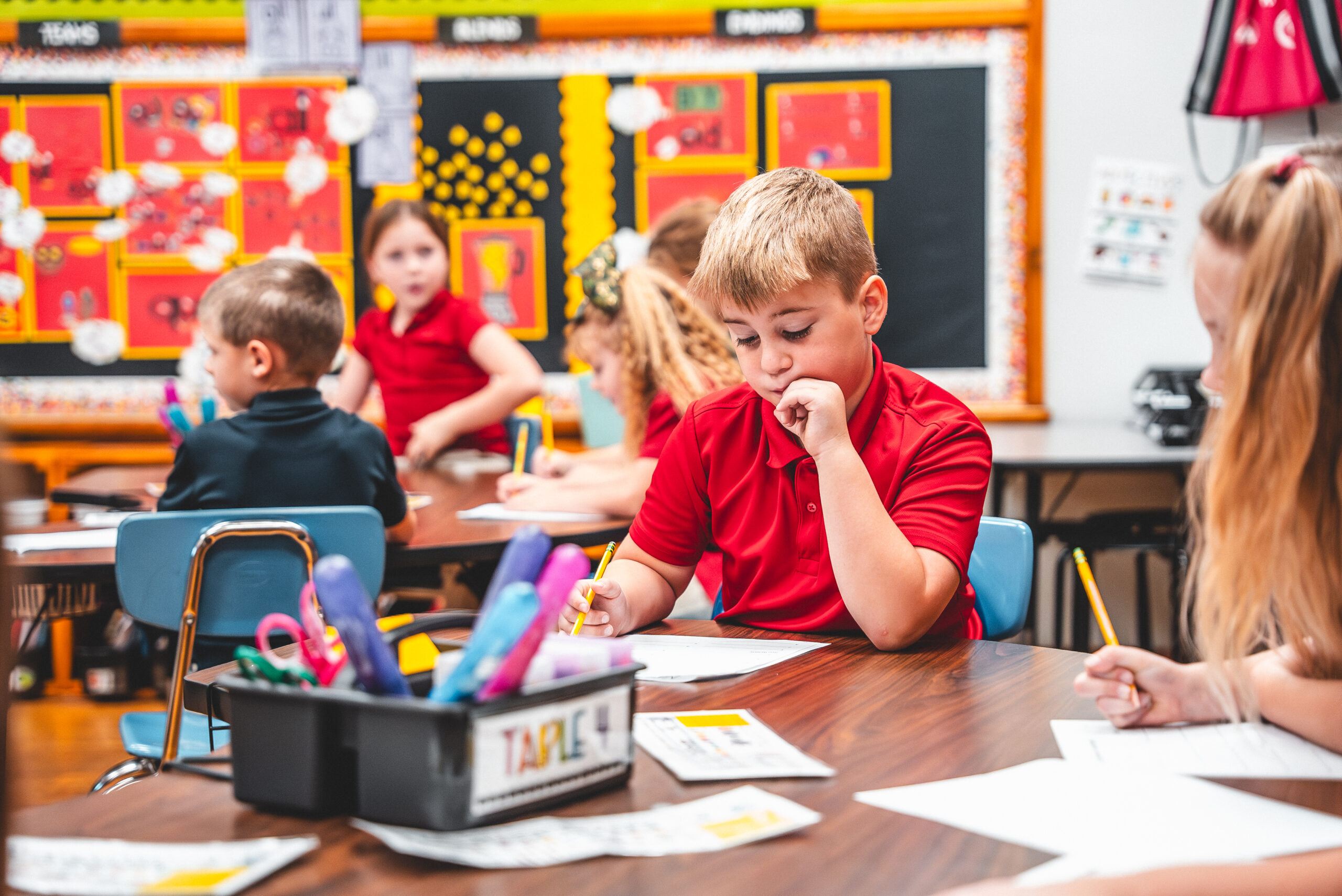 A St. Francis student in a red uniform shirt working at his desk with classmates around him