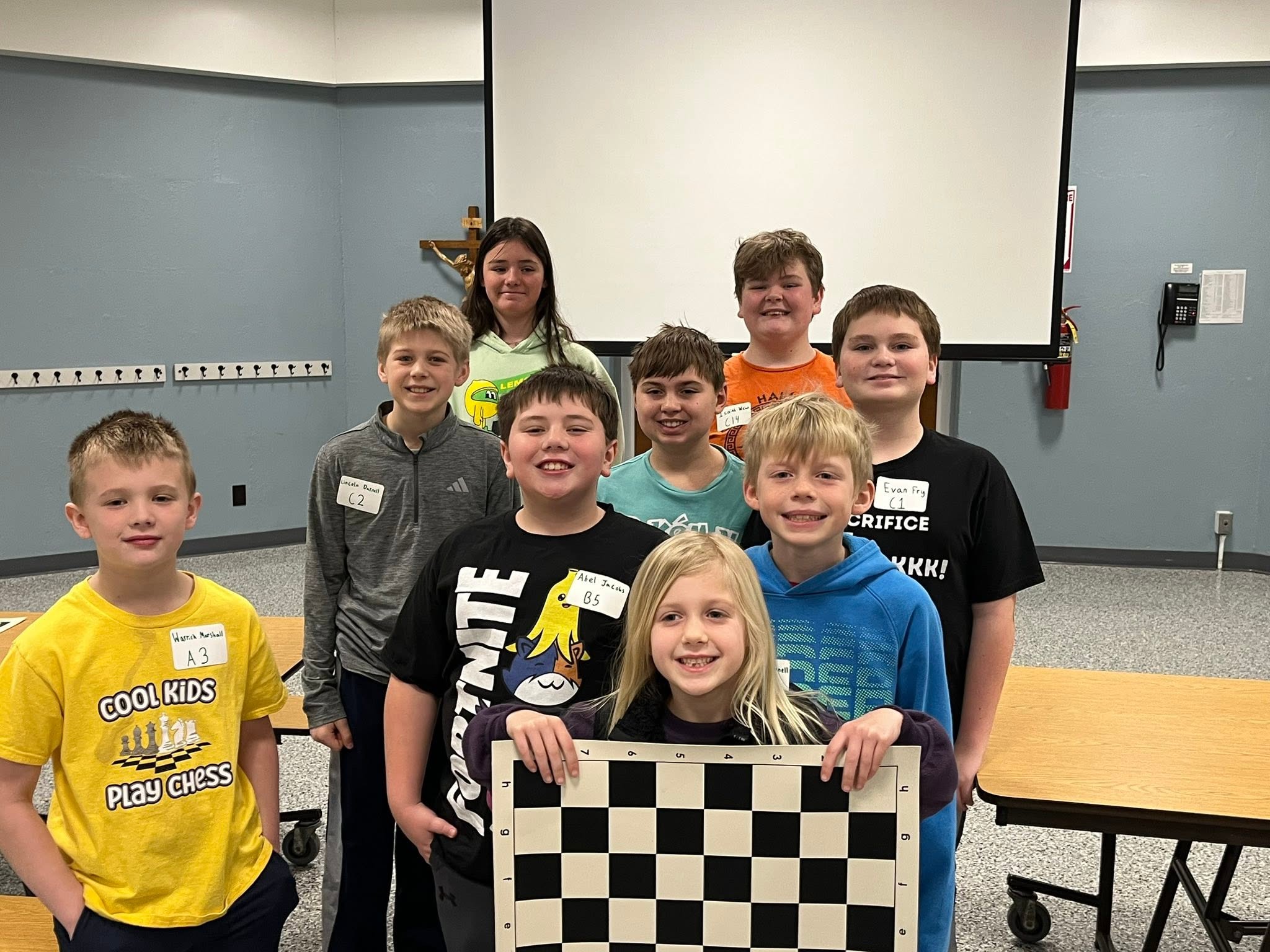 Quincy Catholic Schools Chess Club students smiling together around a large chessboard