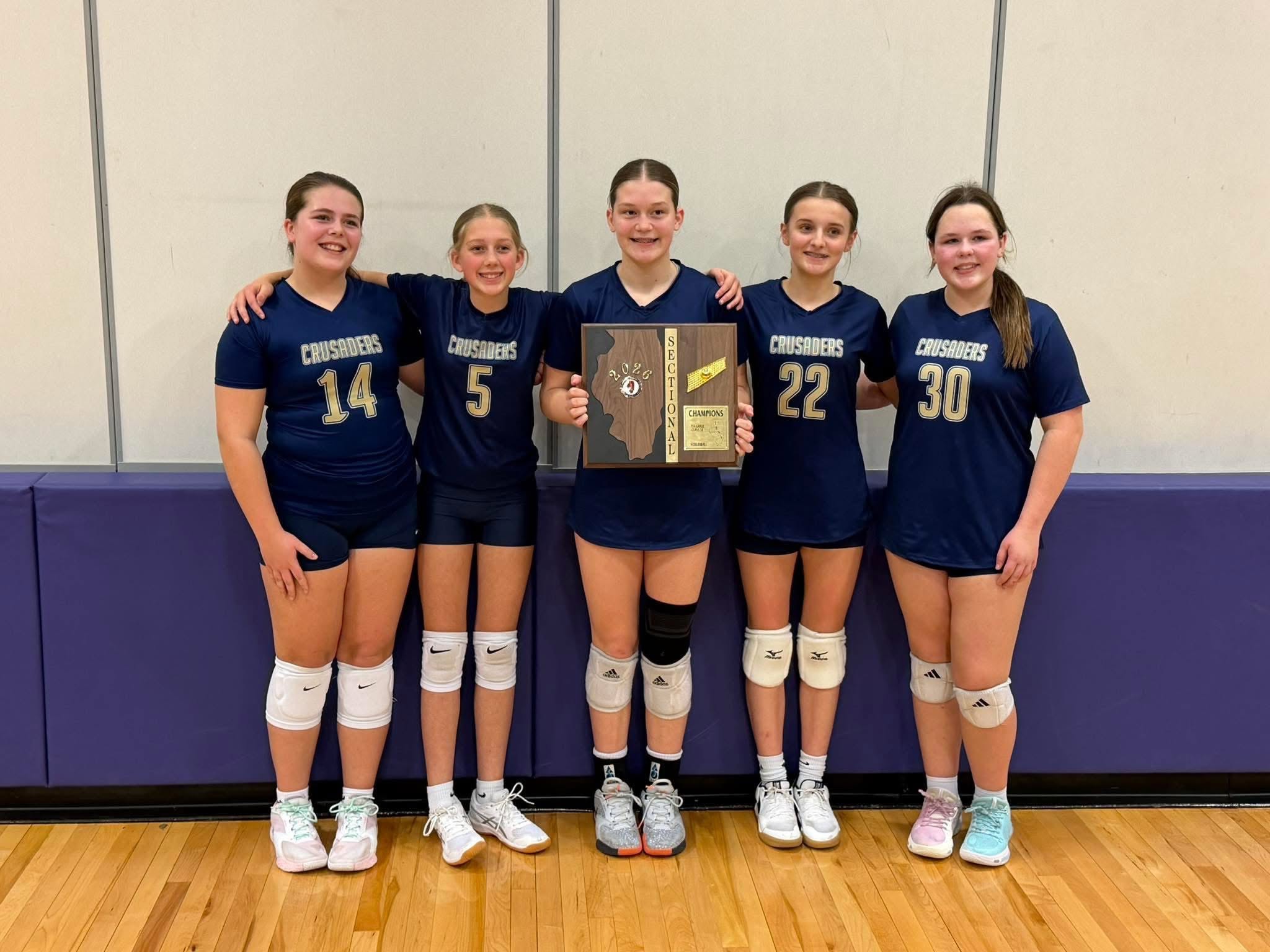 Five Quincy Catholic Crusaders volleyball players in navy uniforms holding their IESA sectional championship plaque