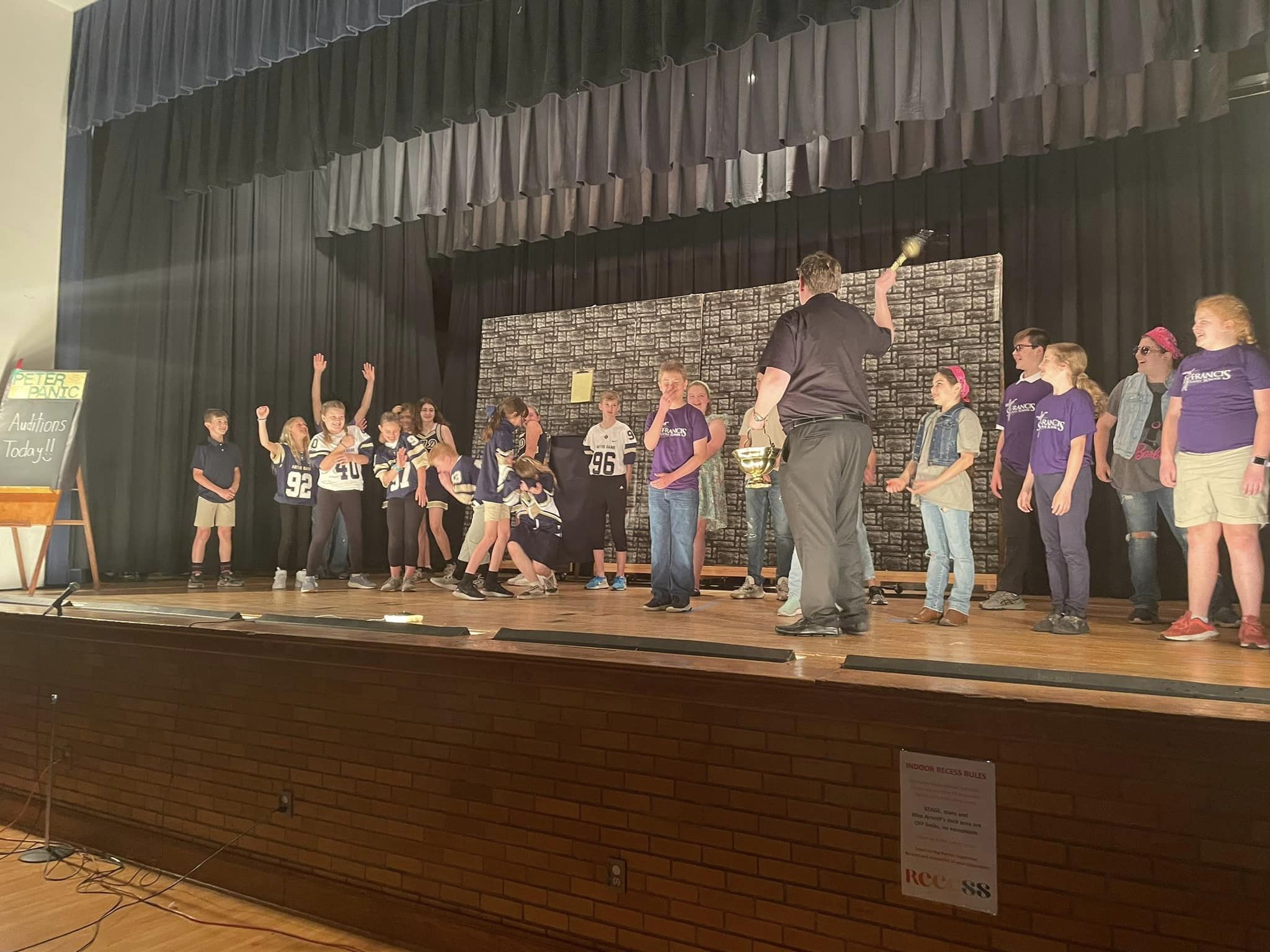 The cast of the St. Francis school play on stage, receiving a blessing before the show
