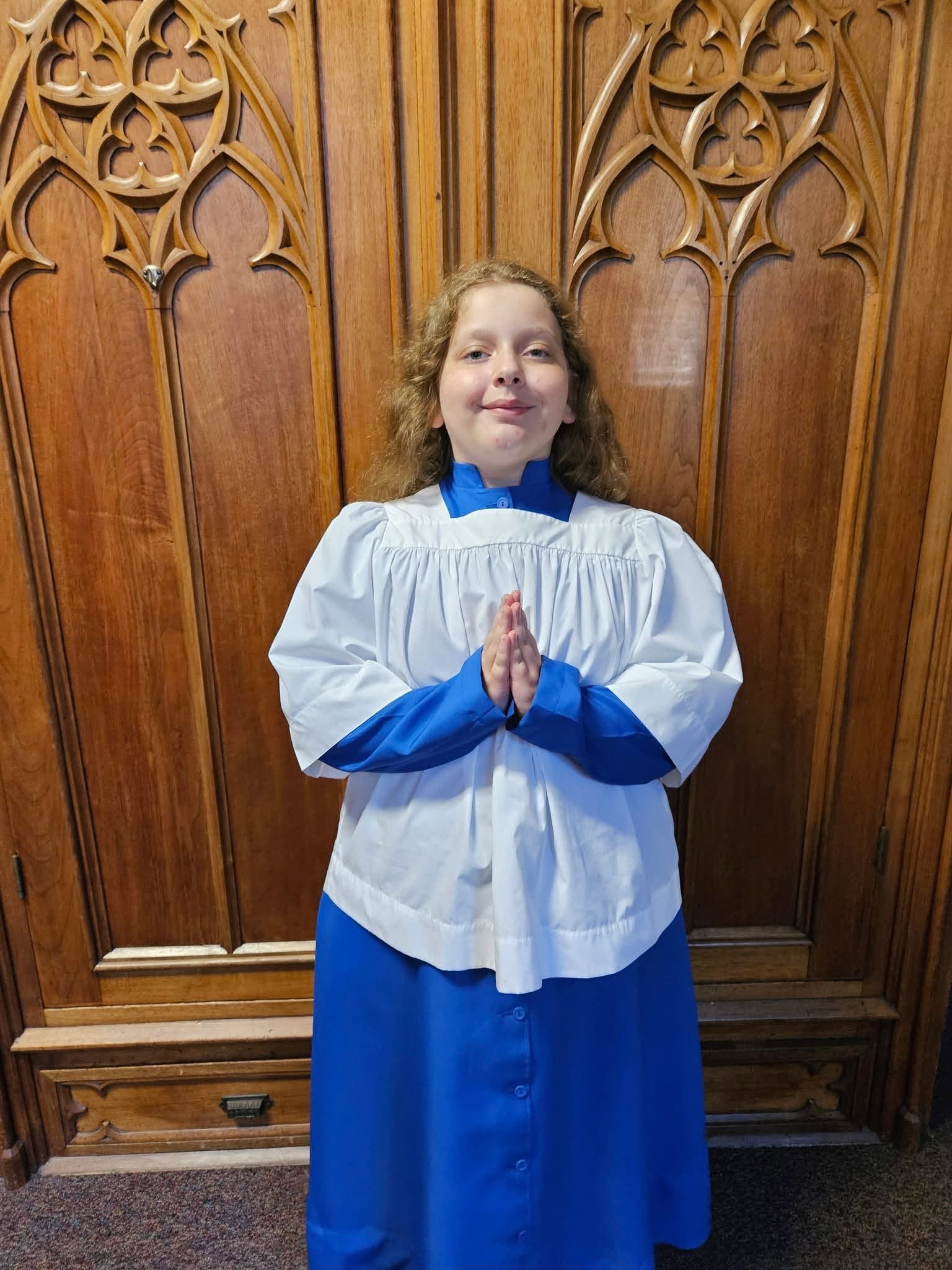 A St. Francis altar server in a white surplice and blue cassock, hands folded in prayer