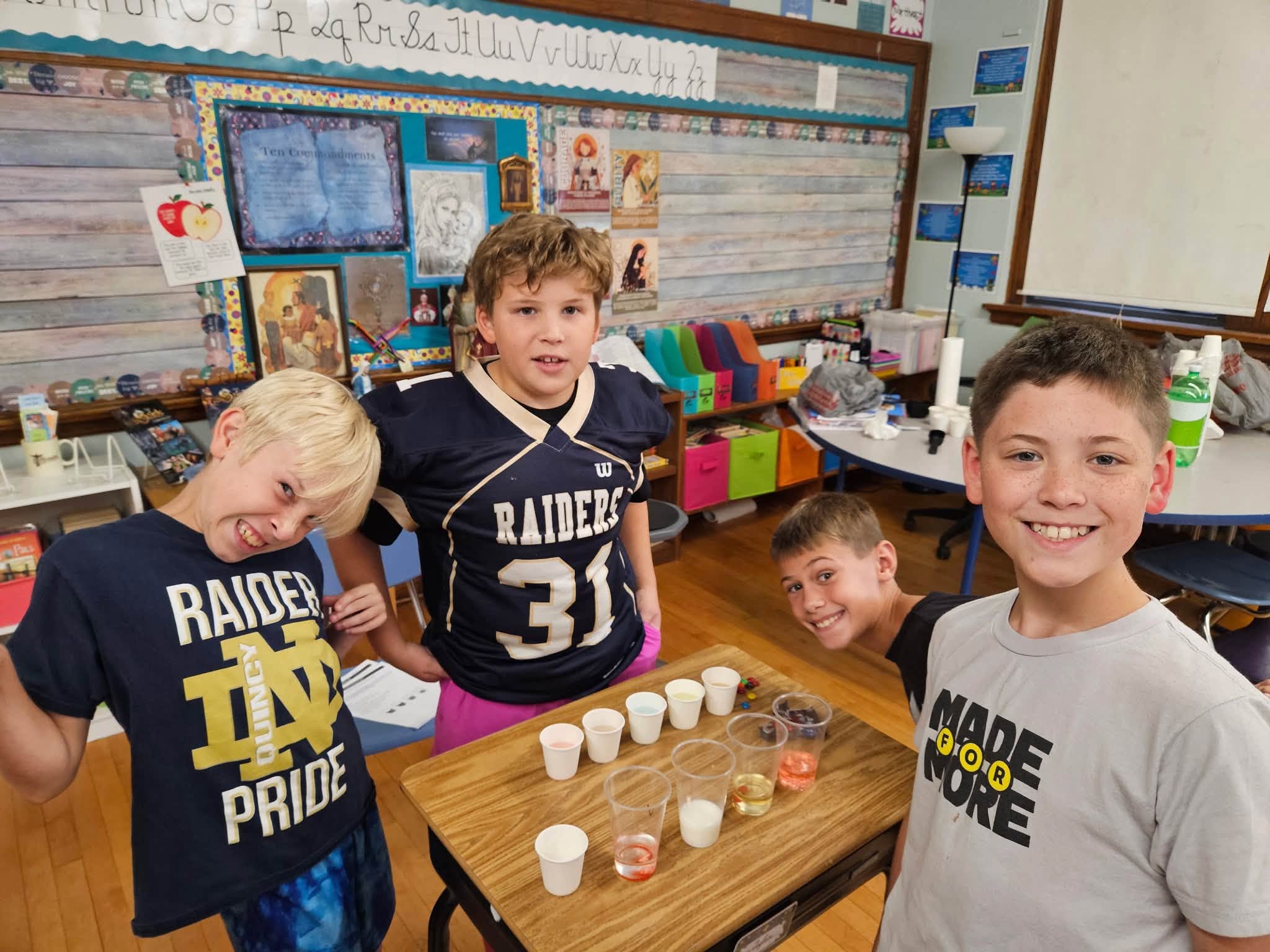 St. Francis boys in Raiders and Notre Dame shirts grinning around a science experiment in their classroom